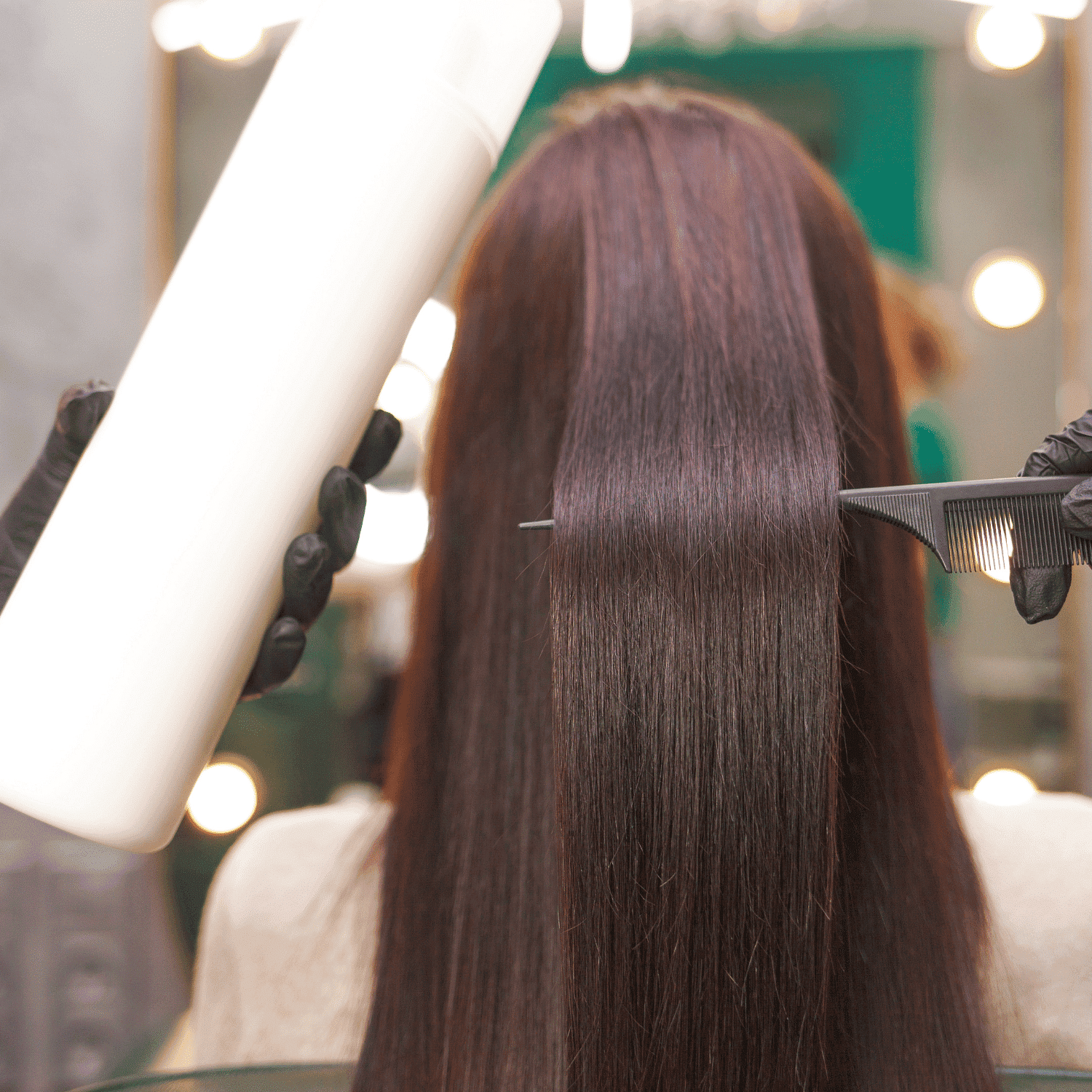 Hairdresser applying product to long brown hair in salon setting.
