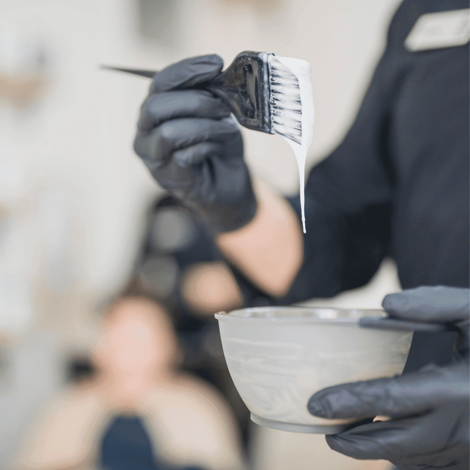 Hairdresser applying hair dye with a brush, holding a bowl, in a salon setting.